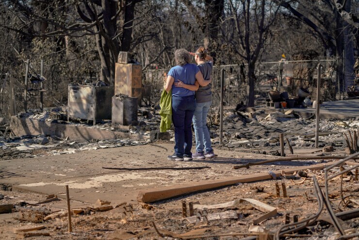 Two women stand looking at their home destroyed by wildfire in Altadena